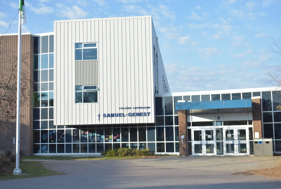 L'entrée principale du Collège catholique Samuel-Genest : une façade vitrée surmontée d'un volume blanc portant le nom de l'école, sous un ciel d'hiver.